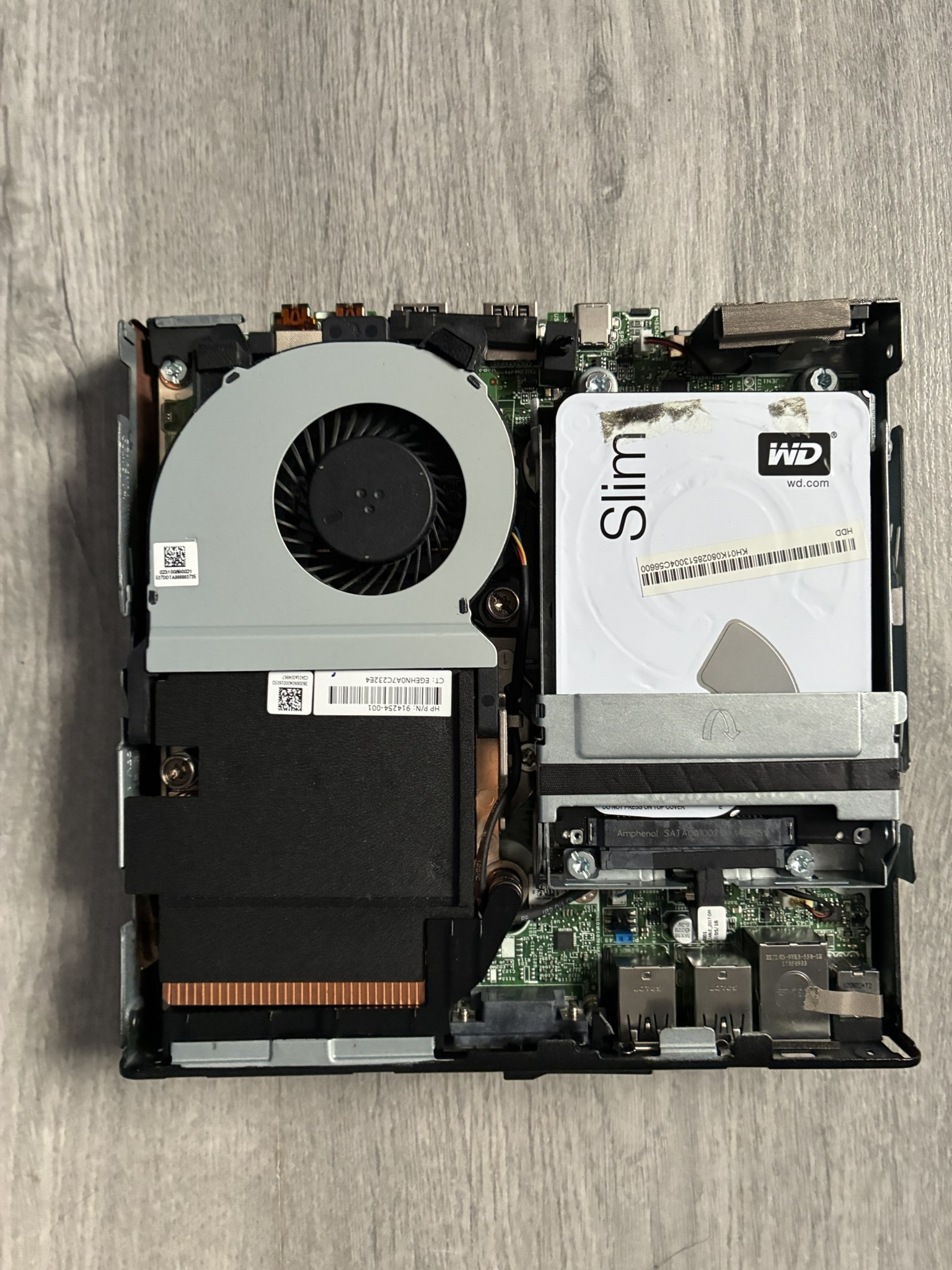 Interior of the HP EliteDesk mini PC with its case open, showing the cooling fan, a 2.5-inch hard drive, and the compact motherboard.